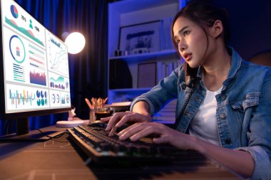 Genç ve güzel Asyalı yaratıcı kadın, gece modern ofisteki bilgisayar analizini ararken strateji pazarlama yaratıcısı planına bilgi vermek için müşteriyi ya da iş arkadaşını telefonla arıyor. Taktik.