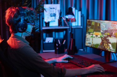 Genç oyun flamasının sunucu kanalı, takım oyuncusu, dijital neon odasında mikrofonlu kulaklık takarak bilgisayar ekranında çoklu oyuncuyla savaş oyunu oynuyor. Toplayıcı.