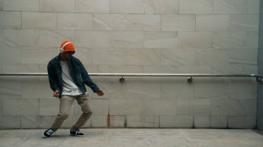 Asyalı akıllı hipster, kulaklık ve şık kıyafetler giyip hip hop şarkıları dinlerken gri arka planlı enerjik break dans gösterisi yapıyor. Açık hava sporu 2024. Hip hop hareketi. Yumuşak bir şekilde..
