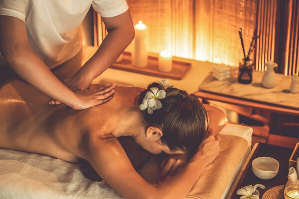 Caucasian woman customer enjoying relaxing anti-stress spa massage and pampering with beauty skin recreation leisure in warm candle lighting ambient salon spa at luxury resort or hotel. Quiescent