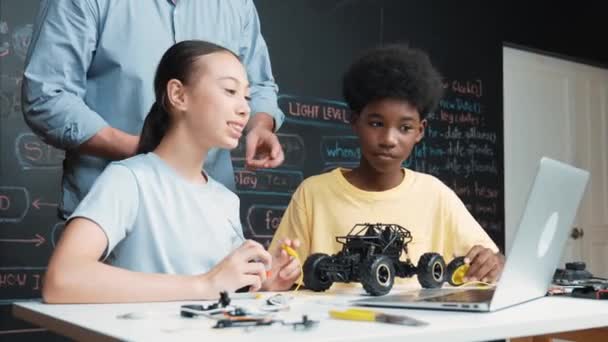 ラップトップ画面を指すコーカサス教師は ブラックボードの車のモデルシステムをコーディングやプログラミングコードで説明します ロボット工学について学ぶ多種多様な学生 イスラーム主義 — ストック動画
