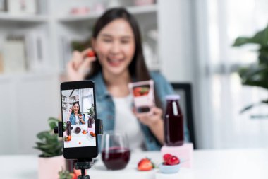 Seçici odaklı akıllı telefon ve gülümseyen genç, güzel Asyalı karışık çilek ve kiraz suyu detoksu değerlendirmesi sosyal medyada sağlıklı ürün tanıtımı sunuyor. Taktik.