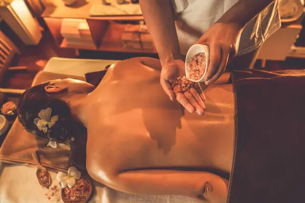 Woman customer having exfoliation treatment in luxury spa salon with warmth candle light ambient. Salt scrub beauty treatment in Health spa body scrub. Quiescent