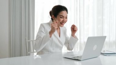 Genç Asyalı iş kadını büyük bir satışı veya başarılı bir iş kampanyasını, başarılı bir gülümsemeyi ve masasında dizüstü bilgisayarla otururken heyecanlı bir yüz ekspresini kutluyor. Vivancy ofis çalışanı kutlama yapıyor