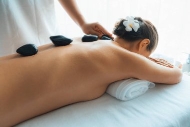 Lüks tatil köyündeki kaplıcalarda sıcak taş masajı. Gün ışığı sükunet ortamında, mutlu kadın müşteri bazalt taş masajından zevk alıyor. Rahatlatıcı bir sıcaklıkla vücudun üzerinde süzülüyor. Sessiz.