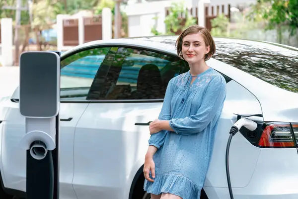 漂亮的年轻女子使用净零排放的替代能源 从家用电动车充电站给电动车充电 现代的年轻姑娘在度假前给她的车子充电 — 图库照片
