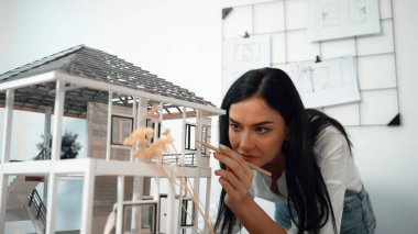 Genç, beyaz, güzel mimar mühendisi ev modelini ev inşaatını teftiş etmek ve sorunu modern ofisteki toplantı masasında çözmek için hata noktasını kontrol etmek üzere çeviriyor. - Yakın çekim. Tertemiz..