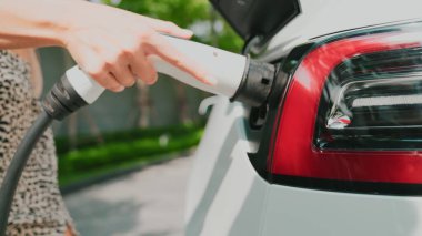 Genç bir kadın yazın yeşil sürdürülebilir şehir bahçesinde EV elektrikli arabasıyla seyahat ediyor. Kentsel sürdürülebilirlik yaşam tarzı yeşil temiz yeniden şarj edilebilir enerji elektrikli BEV araç iç organları