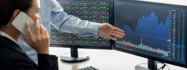 Akıllı işbirlikçi erkek tüccar bilgisayardaki büyüme analizini yatırımcıya gösteriyor. Asyalı iş kadını müşterilerini arıyor. Borsa yatırım kavramı gelişiyor.