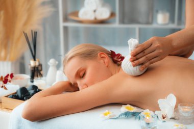 Sıcak bitkisel top spa masaj vücut tedavisi, masör kadın vücuduna nazikçe şifalı bitki torbası bastırıyor. Aromaterapi dinlenme sükuneti ve sükuneti kaplıca salonundaki atmosferi aydınlatıyor. Sessiz.