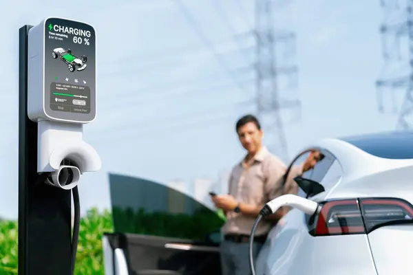 Człowiek Płaci Energię Elektryczną Pomocą Smartfona Podczas Ładowania Akumulatora Samochodowego — Zdjęcie stockowe