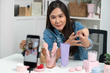 Genç, güzel Asyalı kozmetik makyaj ruju matte pastel rengini modern odadaki sosyal medyada kol testi tanıtımında en çok satanlar listesinde gösteriyor. Taktik.