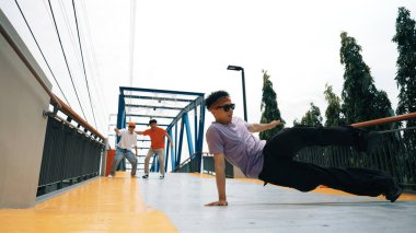 Panorama 'da hipster şık kıyafetler giyer ve dondurucu poz verir. Bir grup profesyonel dansçı break dans yaparken seçkin adam break dans yapıyor. Açık hava sporu 2024. Yumuşak bir şekilde.