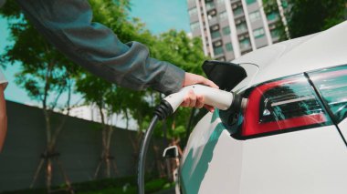 Genç adam EV elektrikli araba aküsünü şehir merkezindeki EV şarj istasyonunda elektrik iç organları için sürdürülebilir yeşil ve yenilenebilir temiz enerji yaşam tarzıyla şarj ediyor.