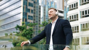 Çatıda müzik dinlerken kulaklık takan profesyonel bir işadamı. Kafkas proje yöneticisi gökdelene bakarken rahatlatıcı müziğe yöneliyor ve yeşil şehirde duruyor. Yaşam tarzı. Urbane.