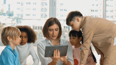 Bir grup öğrenciye çevrimiçi ders verirken elinde tablet tutan akıllı öğretmen. Yetenekli eğitmen mühendislik derslerini anlatırken genç öğrenci oturuyor ve sunumu dinliyor. Etkinlik.