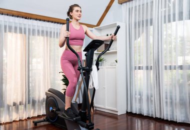 Spor ve atletik bir kadın, evdeki fiziğe ve sağlıklı spor yaşam tarzına uygun vücut egzersizi sırasında eliptik koşu makinesiyle koşuyor. Gaiety evde egzersiz eğitimi.