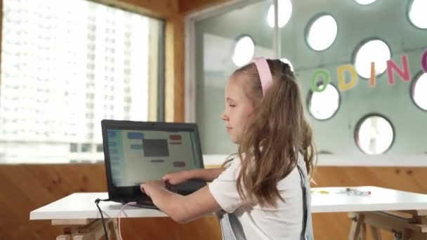 ラップトップを使った笑顔の女の子が 親指をカメラに向けて回ってくる Stemテクノロジー教育でラップトップライティングコードを使用しながらヘッドフォンを着用しているかわいい子供 オンライン学習 エラー — ストック動画