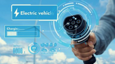 Kameranın önüne odaklanmış EV şarj cihazı bulanık iş adamlarının el rüzgar türbini çiftliği ile batarya durum hologramını gösteriyor. Karbondioksit salınımını azaltmak için temiz enerji kullanan elektrikli araba şarjı tıpası.