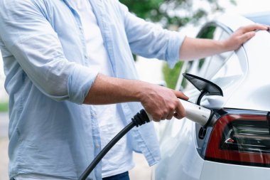 Çevre dostu bilinçli adam EV şarj istasyonundan modern elektrikli aracı şarj ediyor. EV araba teknolojisi gelecekteki sürdürülebilirlik için alternatif ulaşım aracı olarak kullanılıyor. Eşzamanlama