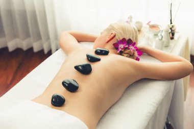 Lüks tatil köyündeki kaplıcalarda sıcak taş masajı. Gün ışığı sükunet ortamında, mutlu kadın müşteri bazalt taş masajından zevk alıyor. Rahatlatıcı bir sıcaklıkla vücudun üzerinde süzülüyor. Sessiz.