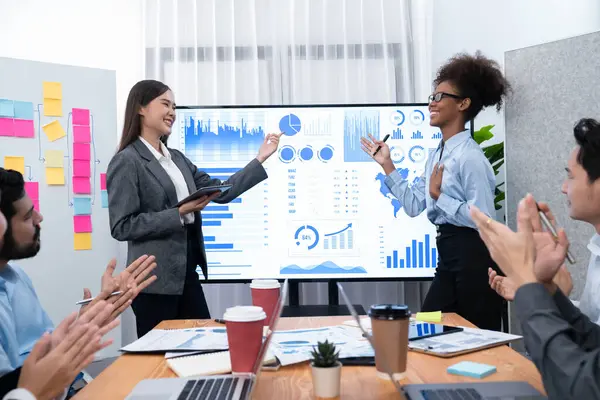 İş adamları TV ekranında başarılı bir sunum veya veri analizi toplantısından sonra kutlama yapıyorlar. Mutlu takım ofis odasında toplanıyor, kutlama jestleriyle işbirliği için tezahürat yapıyorlar. Uyum