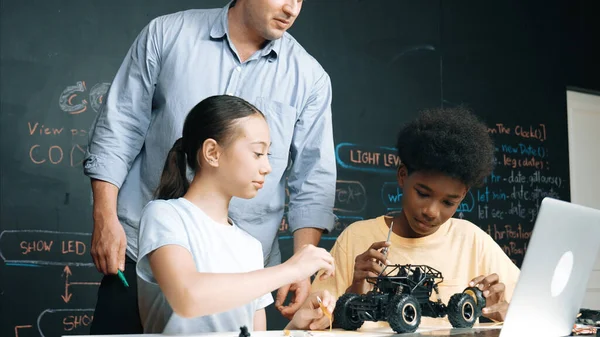 コーディングやプログラミングコードでブラックボードで車のモデルシステムを説明しながら ラップトップ画面を見ているコーカサス教師 ロボット工学について学ぶ多種多様な学生 イスラーム主義 — ストック写真