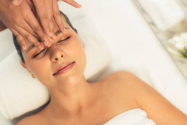 Панорама вид сверху на женщину, наслаждающуюся расслабляющим анти-стрессовым массажем головы и балующим отдыхом кожи лица в дневном спа современном светлом окружении на роскошном курорте или в спа-салоне отеля. Quiescent