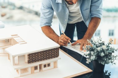 Modern ofisteki mimari aletleri kullanarak ev modelini ölçen profesyonel mühendisin portresini yakından çek. Ev inşaatı, bina planı. Üst Manzara. Eline odaklan. İzleme.