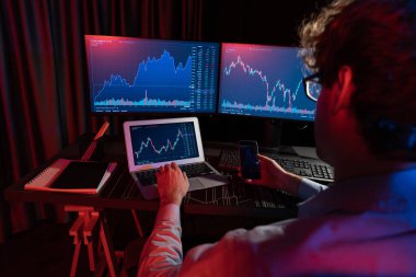 Akıllı telefonlara odaklanan genç tüccar ile piyasa stoku grafiğindeki dizüstü bilgisayarla Neon Light Modern Ofis 'teki gerçek zamanlı ekranları karşılaştırıyor. Dinamik döviz kurunu analiz etme kavramı. Toplayıcı.