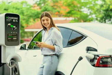 Ulusal Park veya Yaz Ormanı 'ndaki tatil gezisi sırasında EV şarj istasyonundan elektrik aküsü almak için akıllı telefon internet bankacılık uygulaması kullanan genç bir kadın. Yükselt