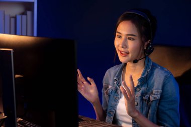 Sunucu kanalı Asyalı etkileyicisi canlı yayında konuşuyor. Sosyal medyada kulaklık takıyor, bilgisayar kaydı yapıyor, dinleyicileri selamlıyor ve Neon Modern Stüdyoları 'nda online olarak koçluk yapıyor. Taktik.