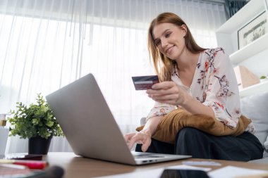 Genç mutlu kadın internetten alışveriş yaparak ürün satın alırken aynı zamanda internet üzerinden online ödeme sistemi ile çevrimiçi mağaza platformundan en yüksek siber güvenlik tarafından korunan ürünler sipariş ediyor.