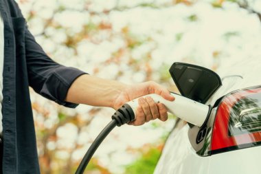 Sonbahar gezisi sırasında sonbahar ormanı arabasında elektrikli araba için şarj eden bir adam. Sonbahar tatilinde elektrikli araçla çevre dostu bir seyahat. Yükselt