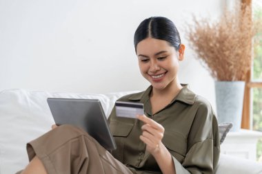 Genç mutlu Asyalı kadın internetten alışveriş yaparak ürün satın alırken aynı zamanda internetten kredi kartıyla online ödemeler sipariş ederek çevrimiçi mağaza platformundan en yüksek sanal güvenlik tarafından korunuyor.