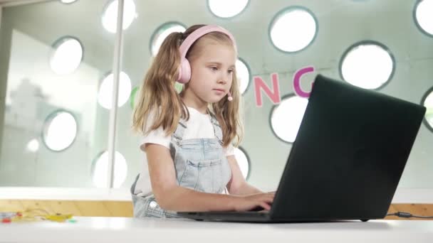 ラップトップやオンライン教室で勉強している若い学生 宿題やリスニングミュージックをしながらラップトップにタイピングする白人少女 ヘッドフォンを着ている小さな子供 クリエイティブ学習 エラー — ストック動画