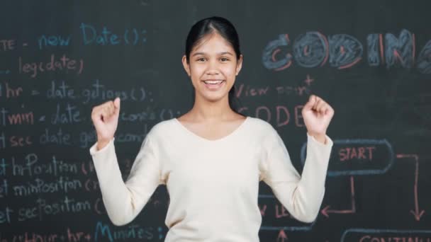 年轻的学生举起胳膊庆祝她的成功计划 快乐的青少年站在黑板前看着相机 用工程代码和写在Stem课堂上的提示 — 图库视频影像