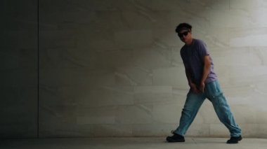 Zeki sokak dansçısı, gri arka planlı bir binada break dansçı hareketi yapıyor. Genç ve çekici koreograf enerjik ve aktif hareket ediyor. Açık hava sporu 2024. Yumuşak bir şekilde..