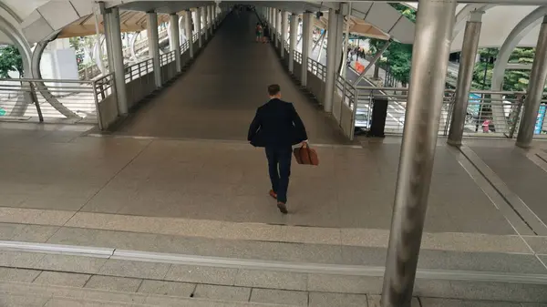 Businessman walking down stair and hurry to walking back to home. Back view of business people wearing suit and celebrate for getting promotion or increasing sales while holding his suitcase. Urbane.