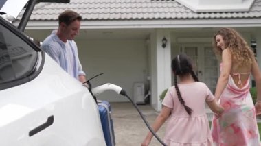 Mutlu küçük kız, ailesinin EV şarj istasyonundan elektrikli aracını şarj etmesine yardım ederken çevre dostu ve enerji sürdürülebilirliğini öğreniyor. EV araba ve modern aile kavramı. Titiz