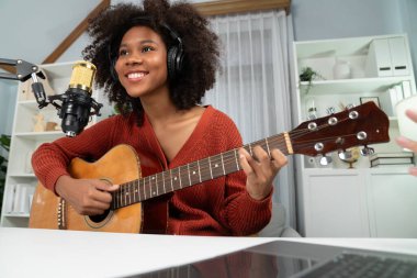 Genç Afrikalı Amerikalı müzisyenin sunucu kanalı gitar çalıyor, şarkı söylüyor, stüdyoda dizüstü bilgisayardan yayın yapıyor. Kulaklık dekorasyonu ve mikrofon kaydı. Tatlandırıcı.
