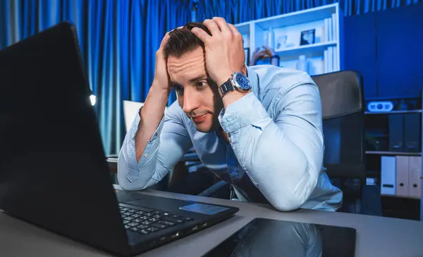 Stressful working businessman waiting email sending back for deadline project at night time, solving issue problem with under high pressure feeling on laptop with at neon light of workplace. Sellable.