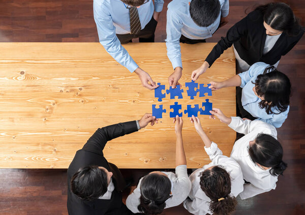 Мультиэтнические бизнесмены держат в руках головоломки и объединяют их как эффективное решение командной работы, общего видения и общей цели, объединяющей разнообразные таланты. Панорама вид сверху. Дотошный