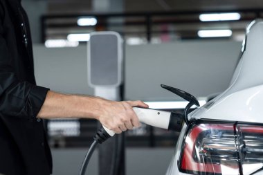 Genç adam EV elektrikli arabasıyla alışveriş merkezinin otoparkına gidiyor şehir merkezindeki şarj oluyor yeşil, temiz, yeniden şarj edilebilir elektrikli araç iç organları ile kentsel sürdürülebilirlik yaşam tarzını gösteriyor