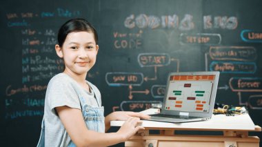 Asyalı öğrenci mühendislik kodları ya da masadaki ekipmanlarla birlikte kameraya doğru dönün. Güvertede dizüstü bilgisayar kullanarak çalışan tatlı bir kız. Yaratıcı eğitim konsepti. Öğretim.