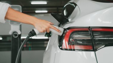 Genç adam EV elektrikli arabasıyla şehir merkezindeki alışveriş merkezinin otoparkına gidiyor şehir merkezindeki sürdürülebilirlik yaşam tarzını yeşil, temiz, yeniden şarj edilebilir elektrikli araç iç organlarıyla şarj ediyor.