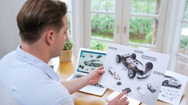 Araba tasarım mühendisi otomobil işi için otomobil prototipini ev ofisinde analiz ediyor. Otomotiv mühendisliği tasarımcısı dikkatle analiz ederek, dizüstü bilgisayarla araba tasarımında kusurlar ve iyileştirmeler buluyor.