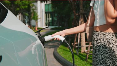 Genç kadın elektrikli taşıtların iç organları için sürdürülebilir yeşil yenilenebilir temiz enerji yaşam tarzına sahip akıllı evdeki konut alanı EV şarj istasyonunda elektrikli araba aküsünü şarj ediyor.