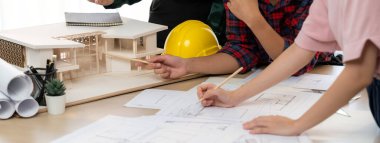 İş arkadaşı mimari belge ve ev modeliyle toplantı masasının planlarını çizerken, profesyonel mimar mühendis ekibinin analiz evi modeli inşaatıyla buluşmasının kırpılmış görüntüsü. Filizlenen.