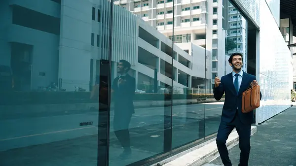 Skilled smart business man dancing with joyful while walking in glass wall. Project manger receive a good news, getting promotion, getting a successful job while express feeling of overjoy. Exultant.